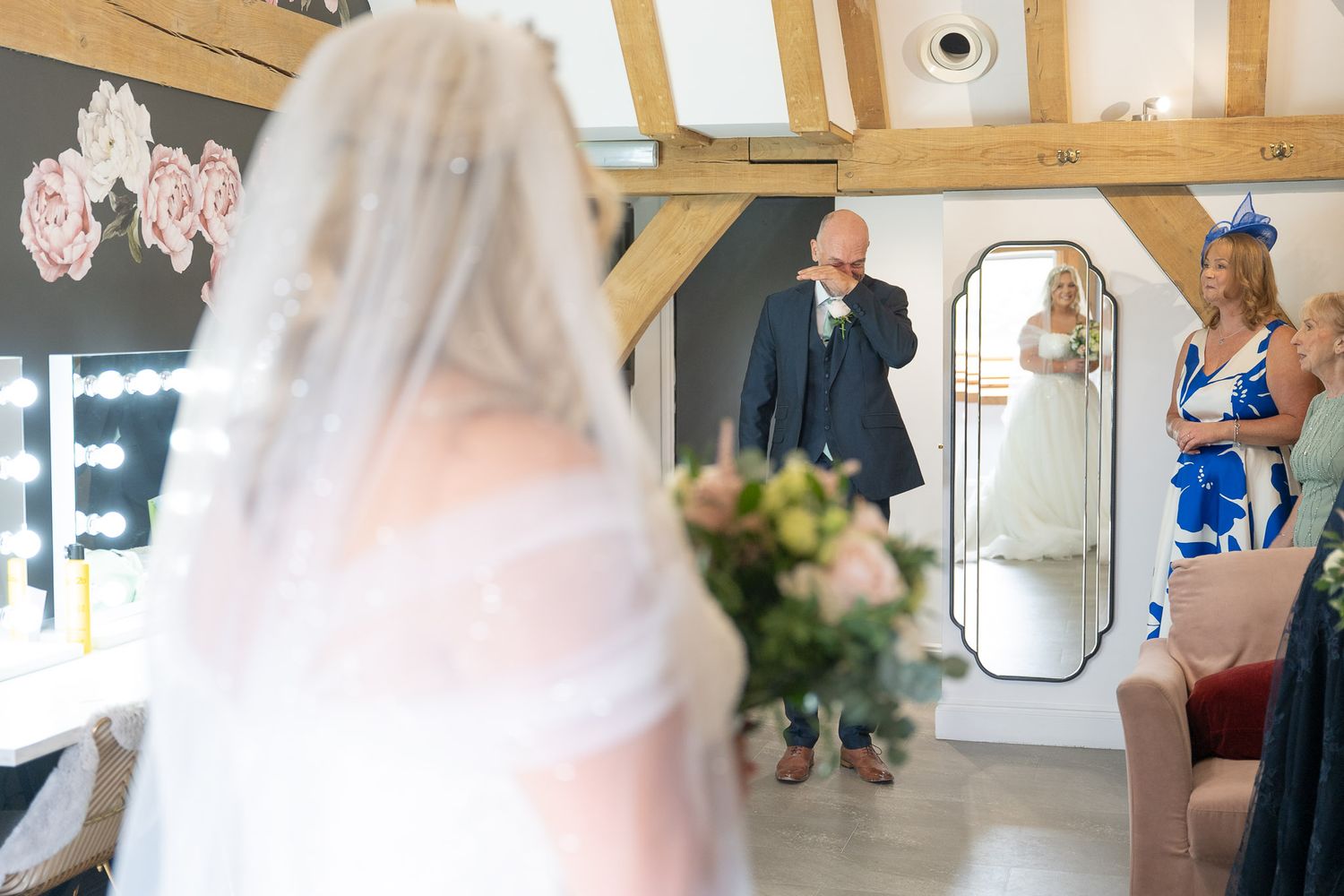 Wedding dress preparations continue as helpers adjust the gown in a sunlit venue space.