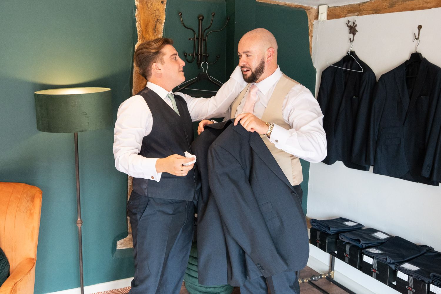 Two people laughing together while getting dressed in formal attire in a dressing room.