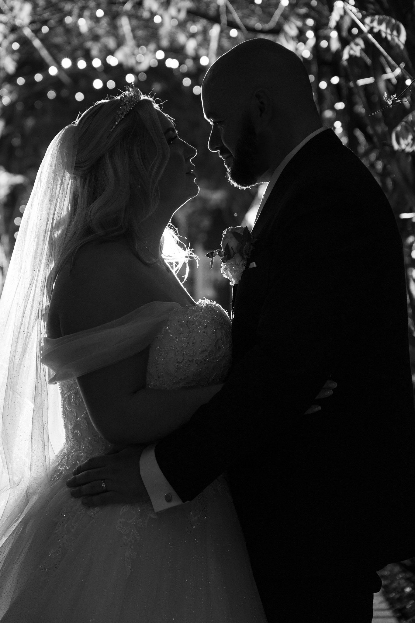 Romantic silhouettes of newlyweds embracing during their first dance under twinkling lights at a wedding reception.