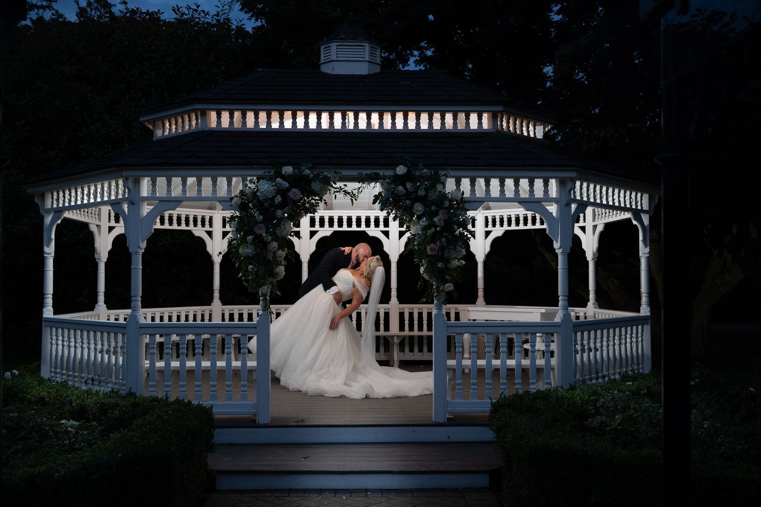 A romantic nighttime wedding photo series showing silhouettes against an illuminated white gazebo in a garden setting.