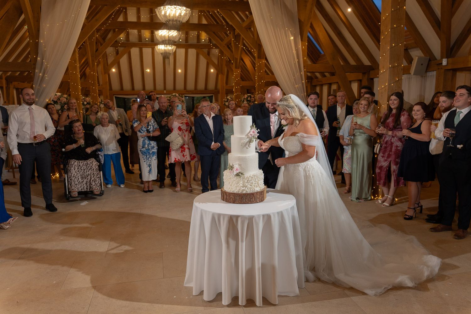 Wedding guests watch as a bride and groom share their first dance in a rustic wooden barn reception venue.