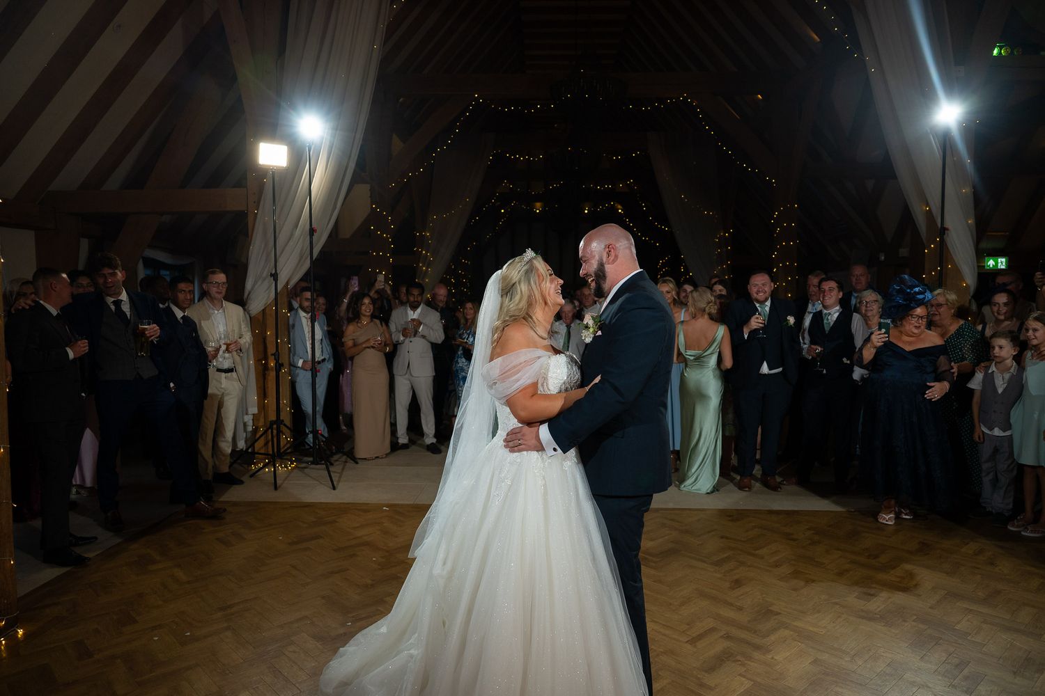 Wedding reception guests dancing and celebrating on a dimly lit wooden dance floor.