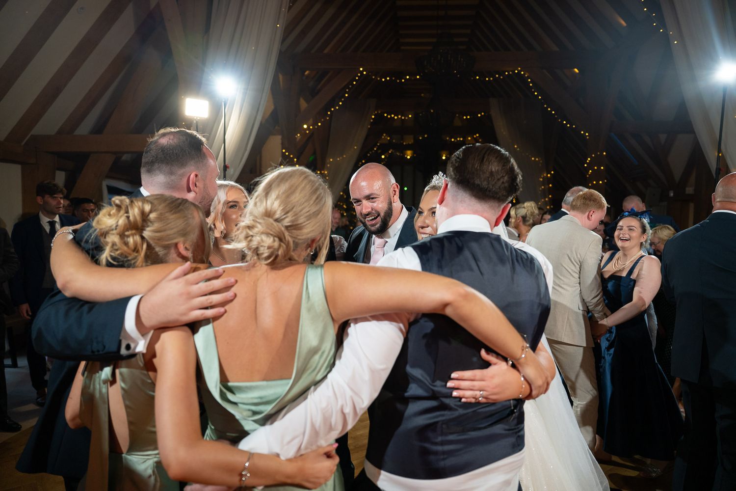 Couples dancing together in a rustic barn venue with twinkling lights and wooden beams overhead.