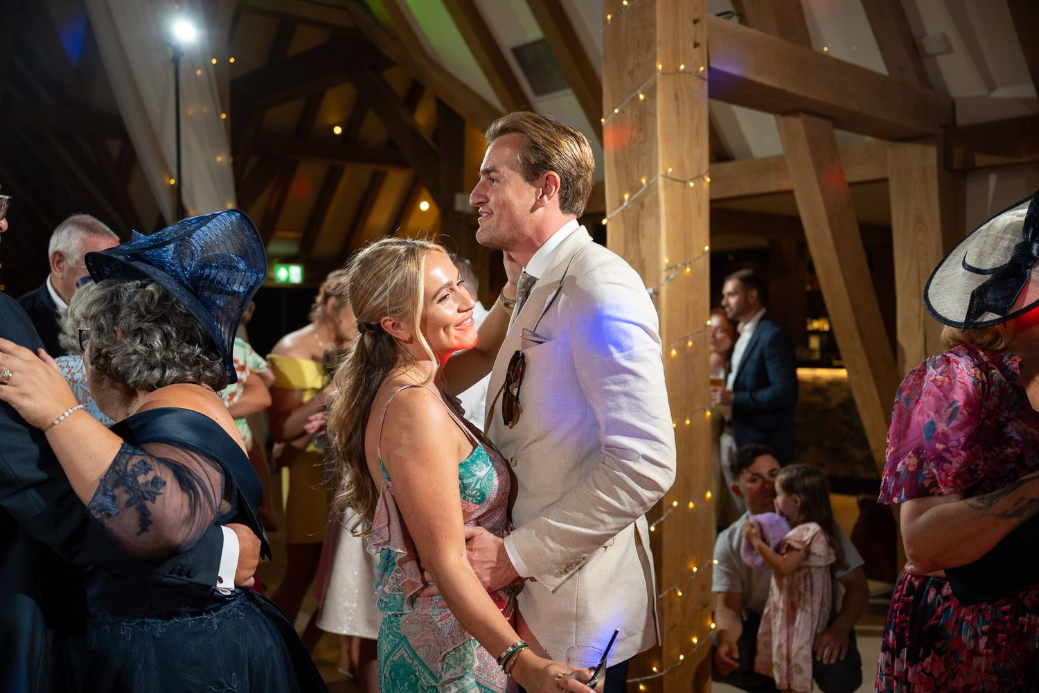 Wedding reception dance party in a barn venue with string lights creating a warm, festive atmosphere.