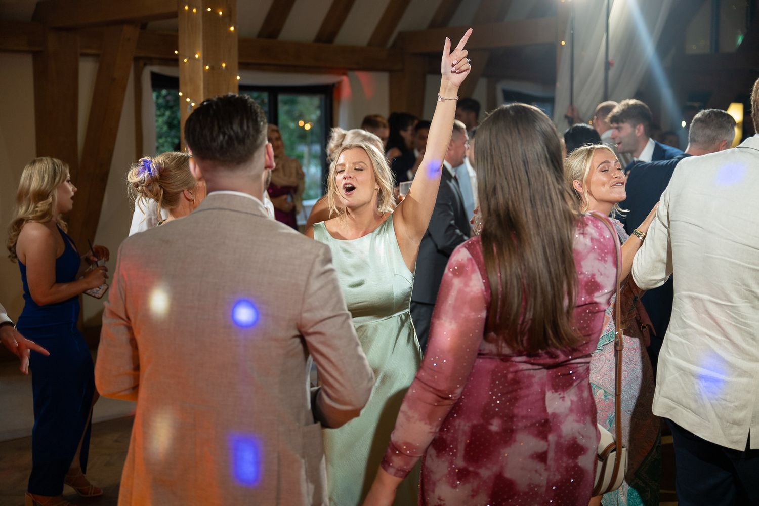 Party guests dance energetically under blue lighting at an indoor celebration event.
