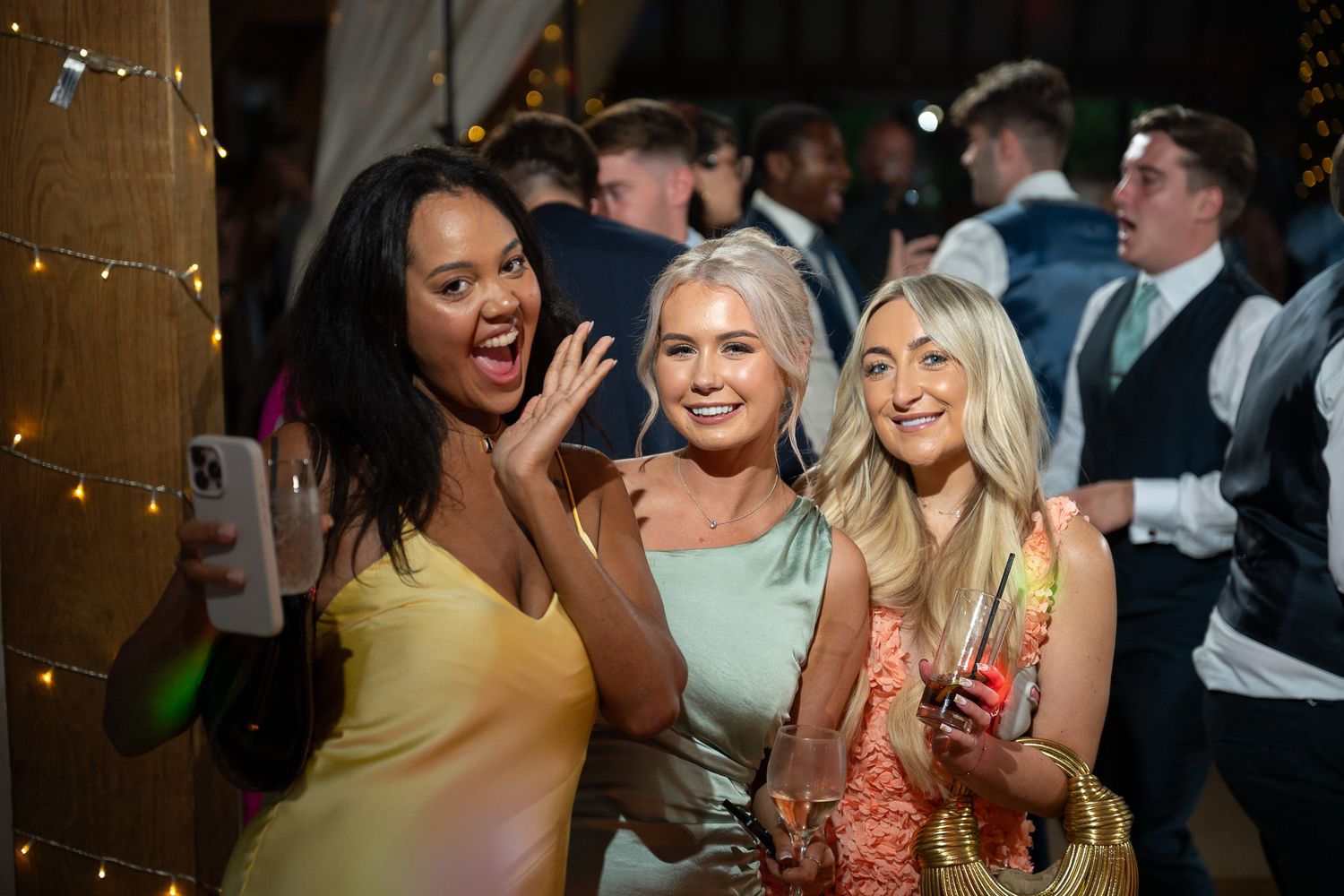 Wedding guests mingle and socialize at a reception with warm lighting and festive atmosphere.