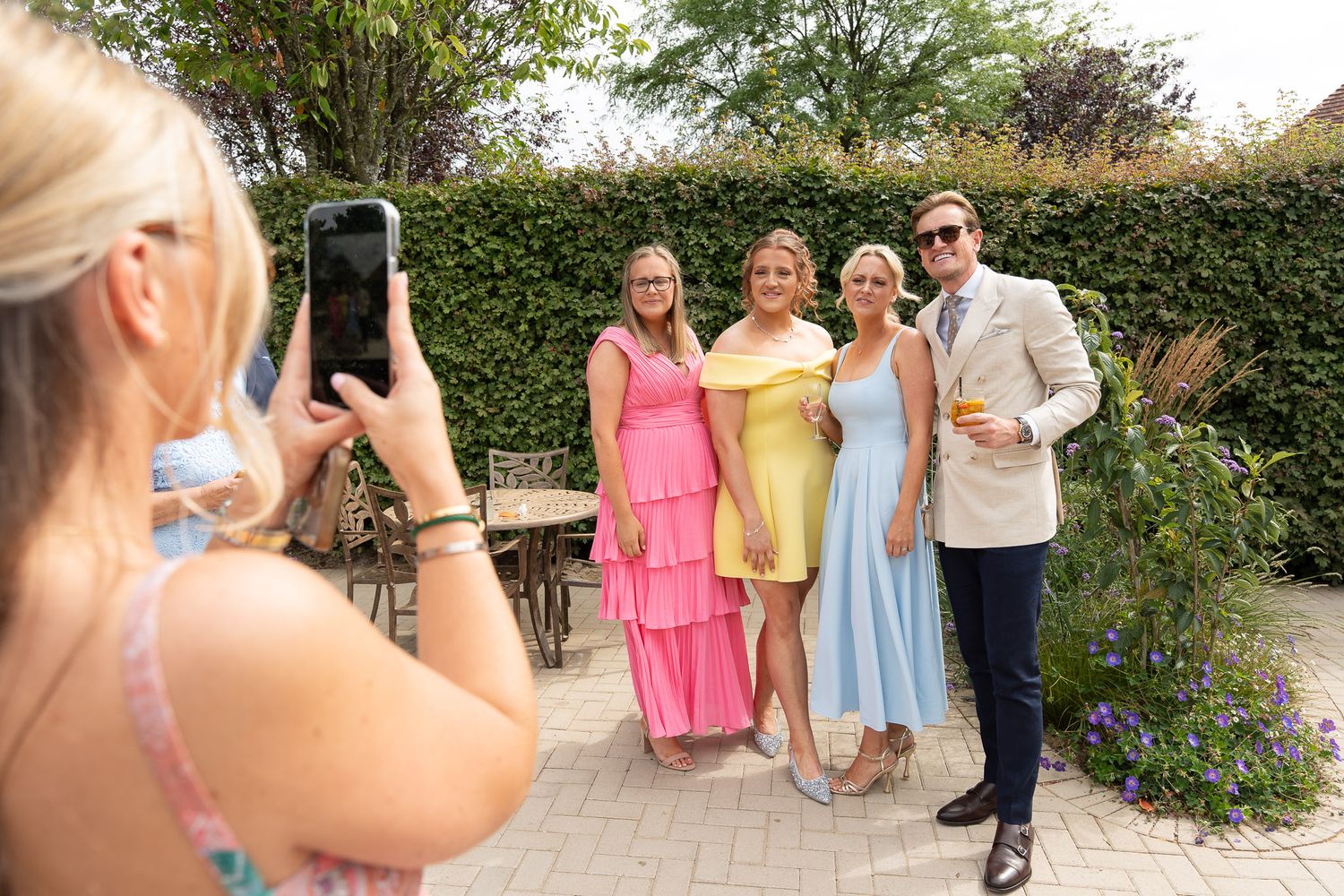 Wedding photographer captures candid moments of bridal party in pastel dresses posing outdoors in garden setting.