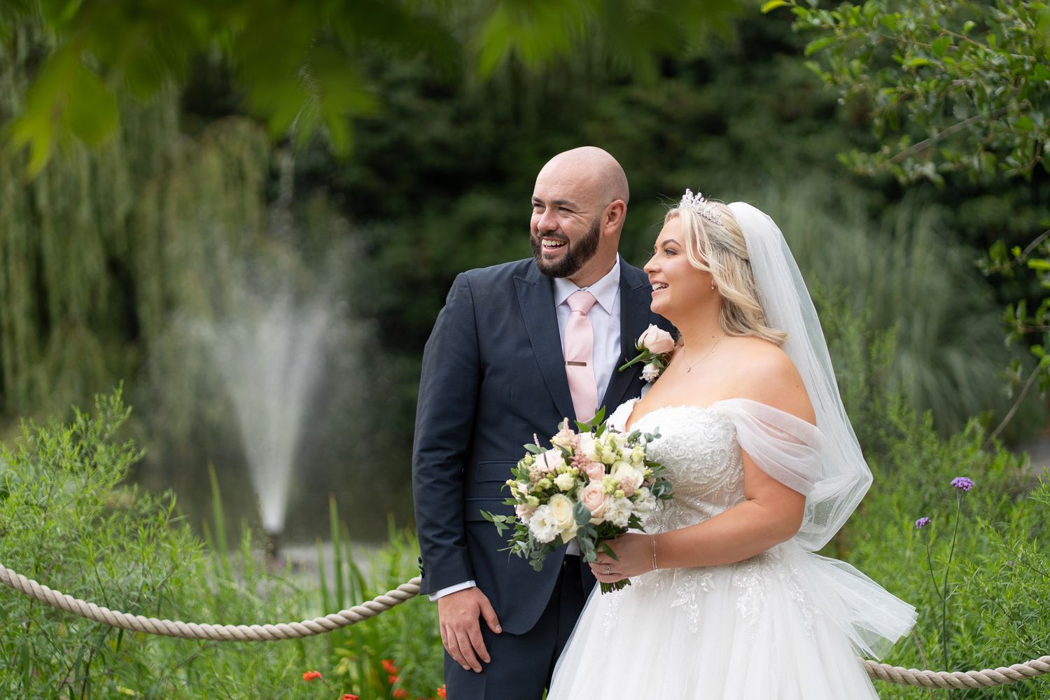 A couple shares a romantic moment during their wedding ceremony in a lush garden setting.