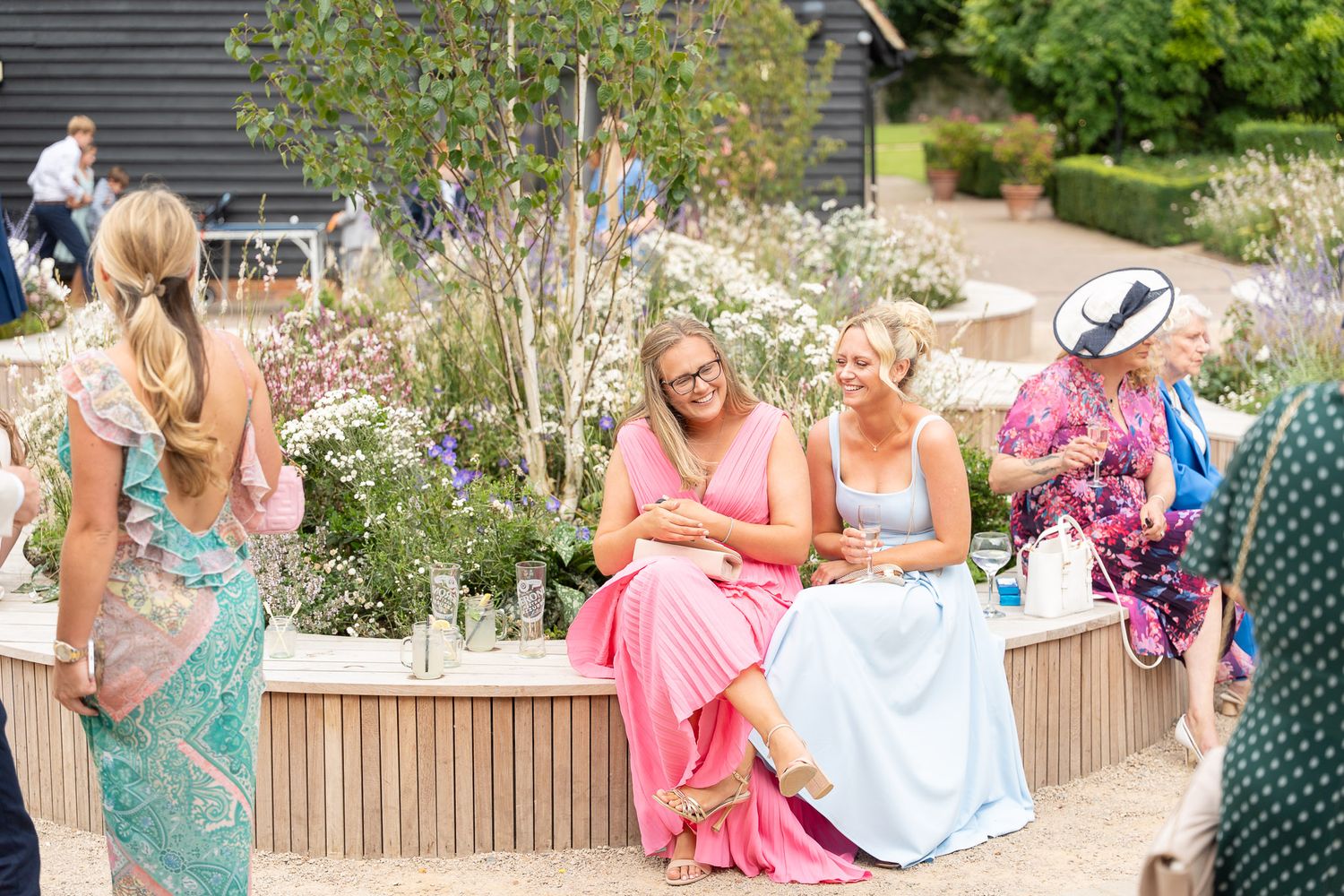 A group celebrates outdoors at a garden party with champagne toasts and festive pink attire.