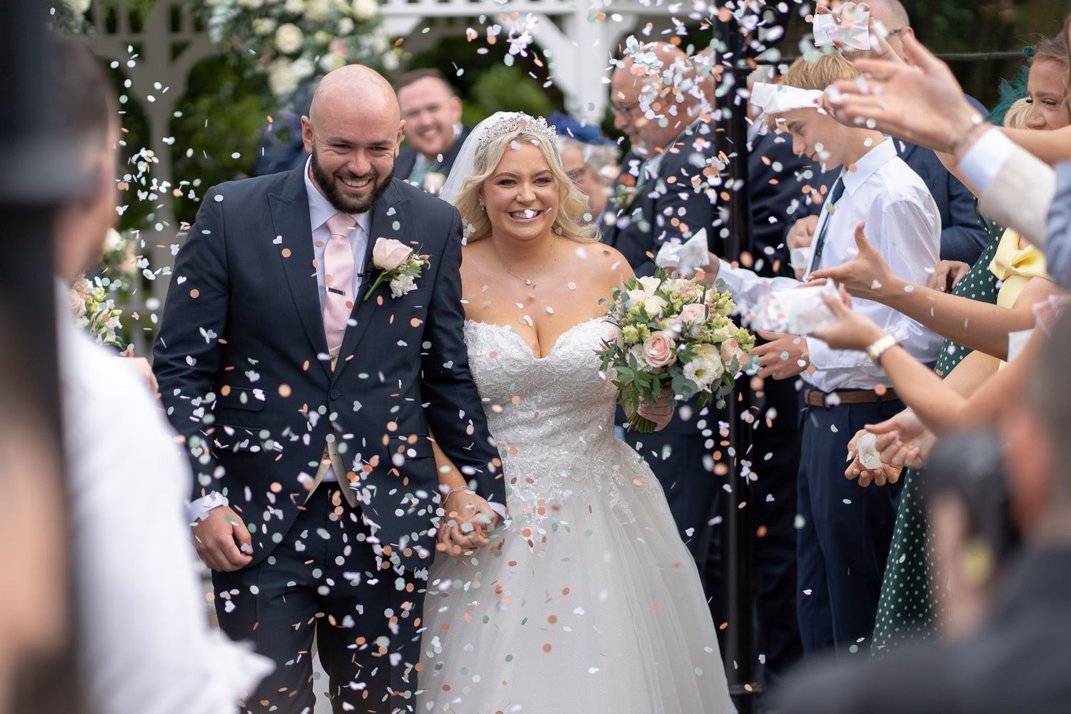 Wedding guests shower newlyweds with white confetti petals during outdoor celebration.