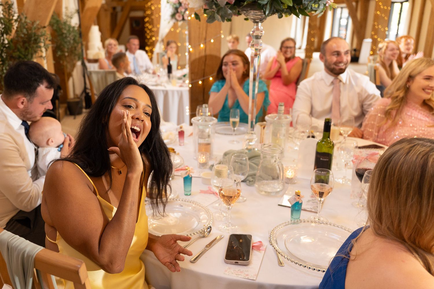 Wedding guests laugh and celebrate during a reception dinner at elegant tables decorated in white linens.
