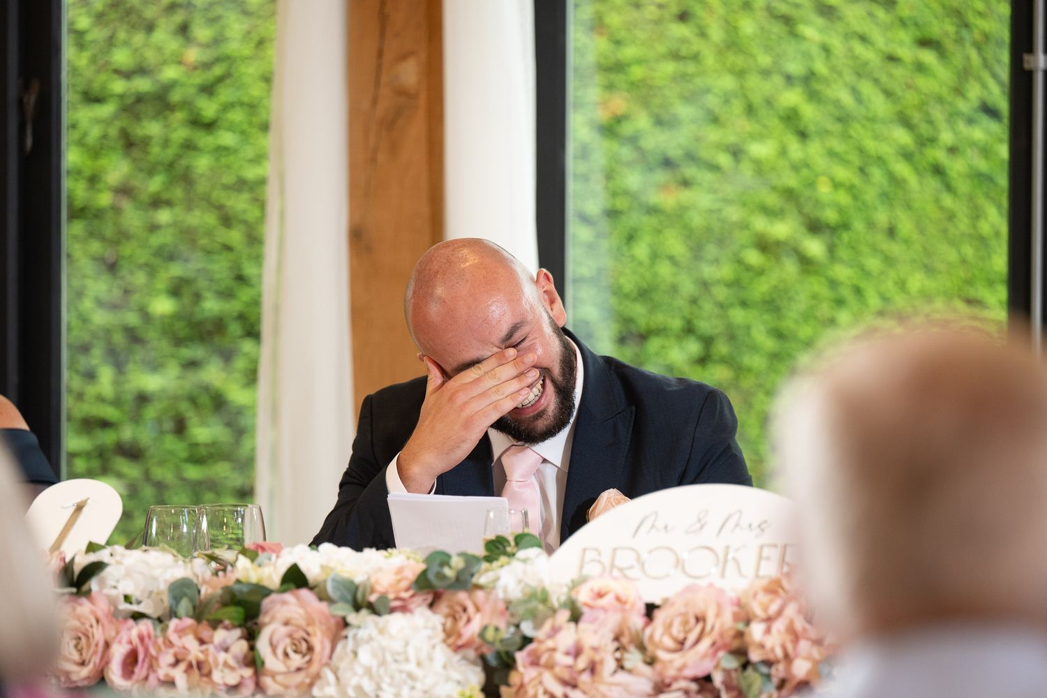 Wedding guests seated at a long table with pink floral centerpieces enjoy a meal during an outdoor reception.