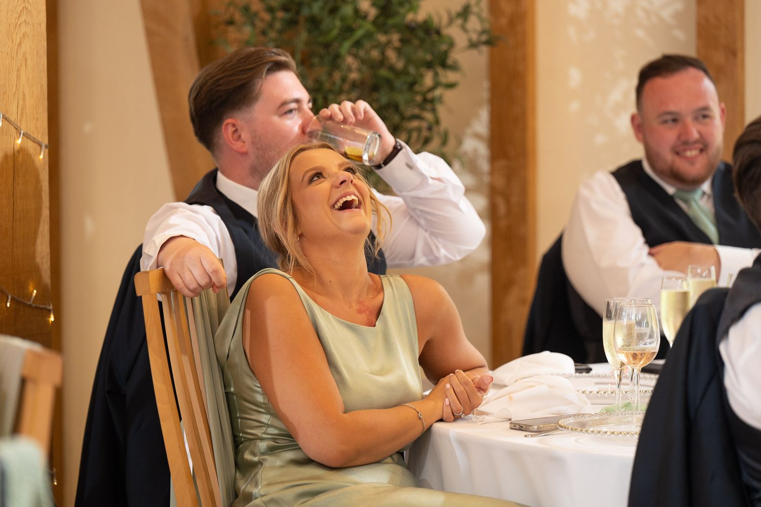 Wedding guests laugh and enjoy themselves during a reception celebration at an elegant indoor venue.