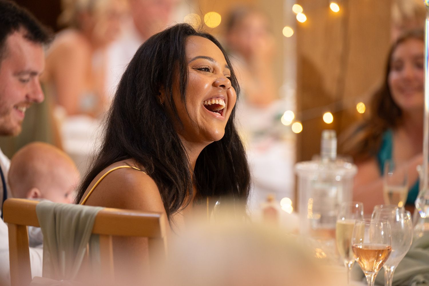 Guests laugh and enjoy themselves at an elegant dinner party with warm lighting and wine glasses on the table.