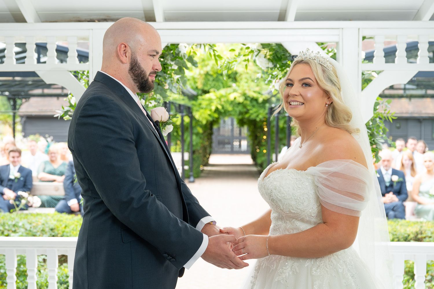 A couple shares a romantic moment during their outdoor wedding ceremony under a white gazebo.