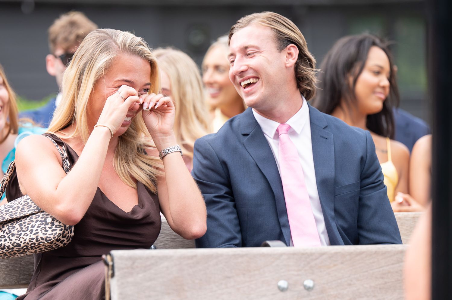 A group of wedding guests react with laughter and joy during an outdoor celebration.