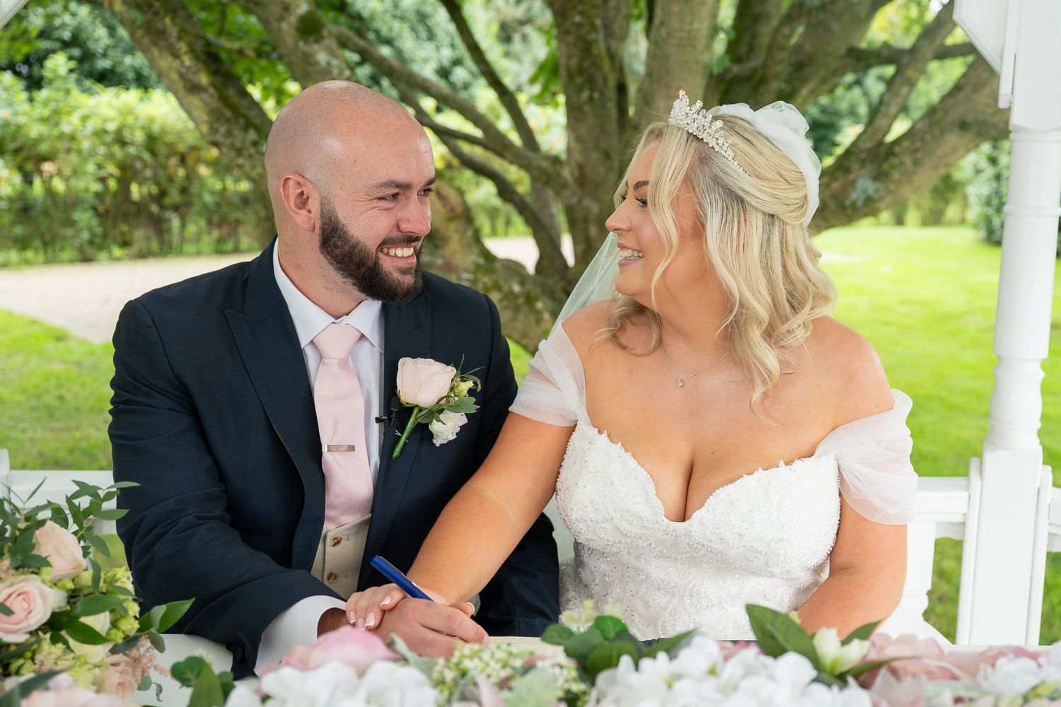 Newlyweds sharing intimate moments during their garden wedding photoshoot under a white gazebo.
