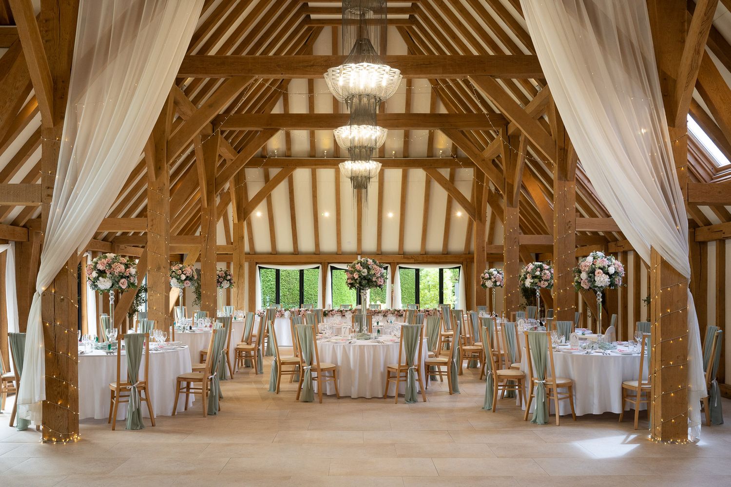 Interior panorama of a rustic wooden barn venue with white drapes and chandeliers set up for an elegant event.