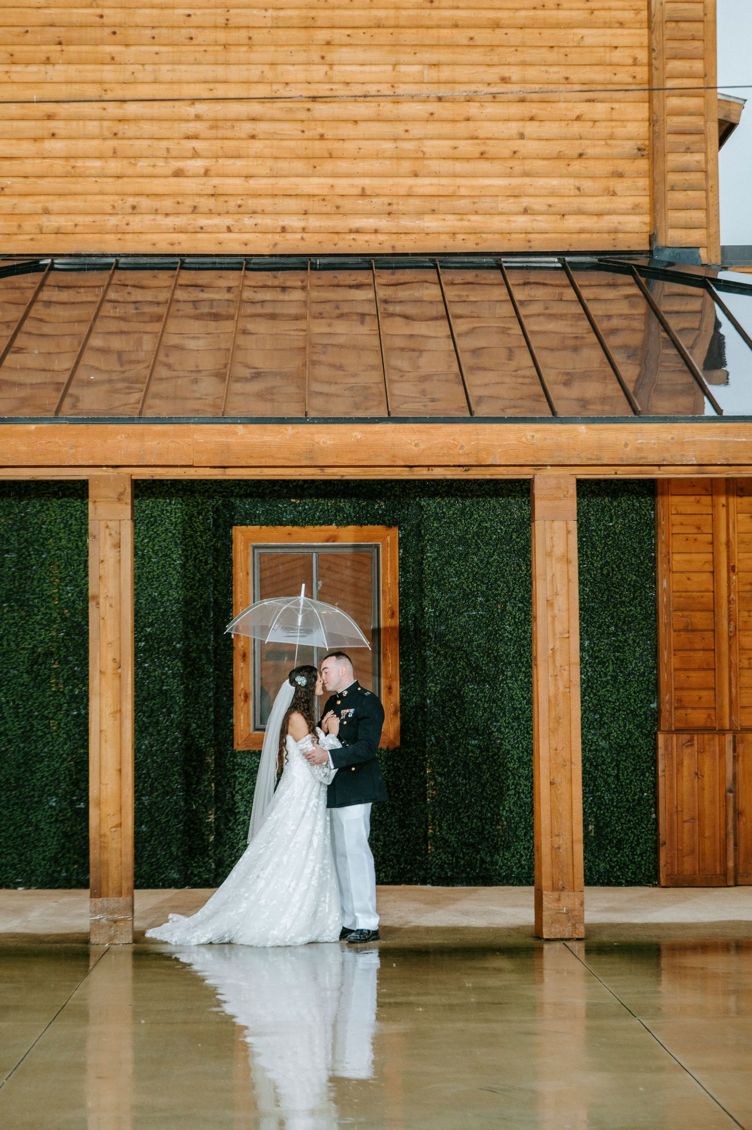Wedding couple dancing and embracing in a rustic wooden venue with artificial grass wall decor.