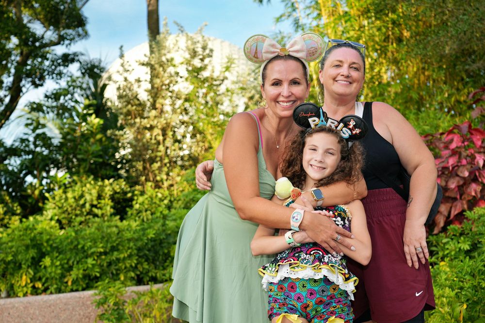 A group of people pose together outdoors in a garden setting with lush greenery and flowers in the background. Epcot Food and Wine festival