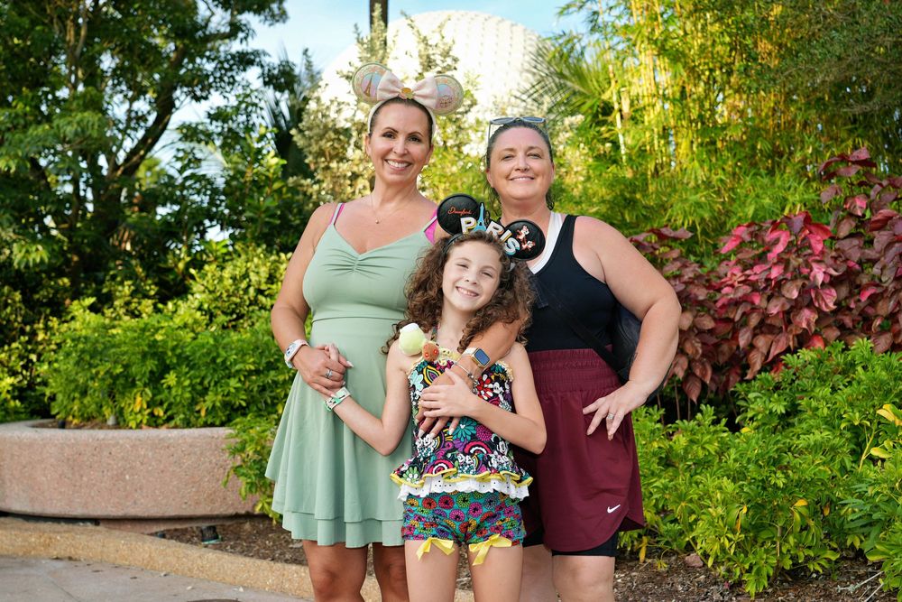 A group of people pose together outdoors in a garden setting with lush greenery and flowering plants in the background.