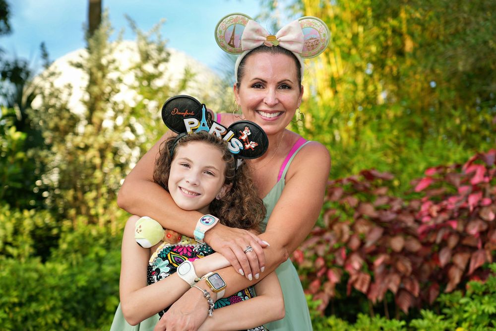 Two people embrace and smile while standing in a lush garden with colorful foliage in the background.