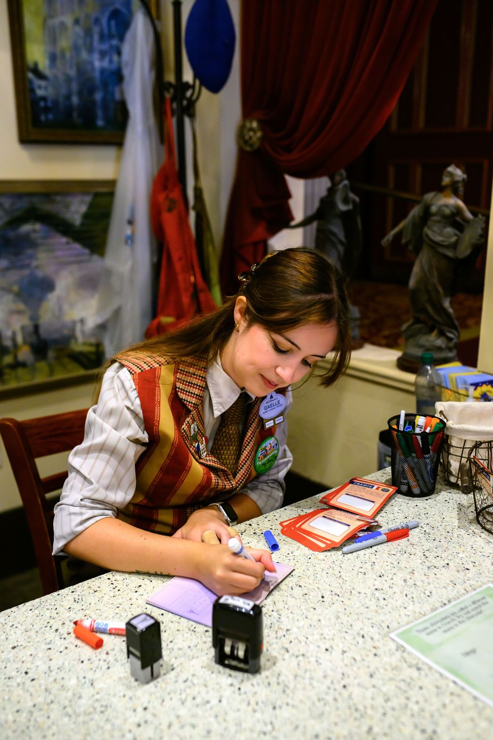 Student wearing a striped shirt and vest works diligently on homework at a speckled table surface.