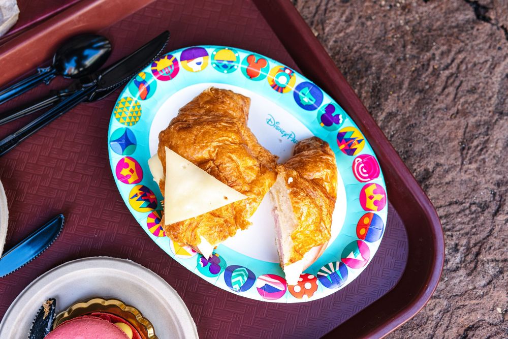 A close-up view of a flaky golden croissant on a colorful floral plate against a dark textured surface.