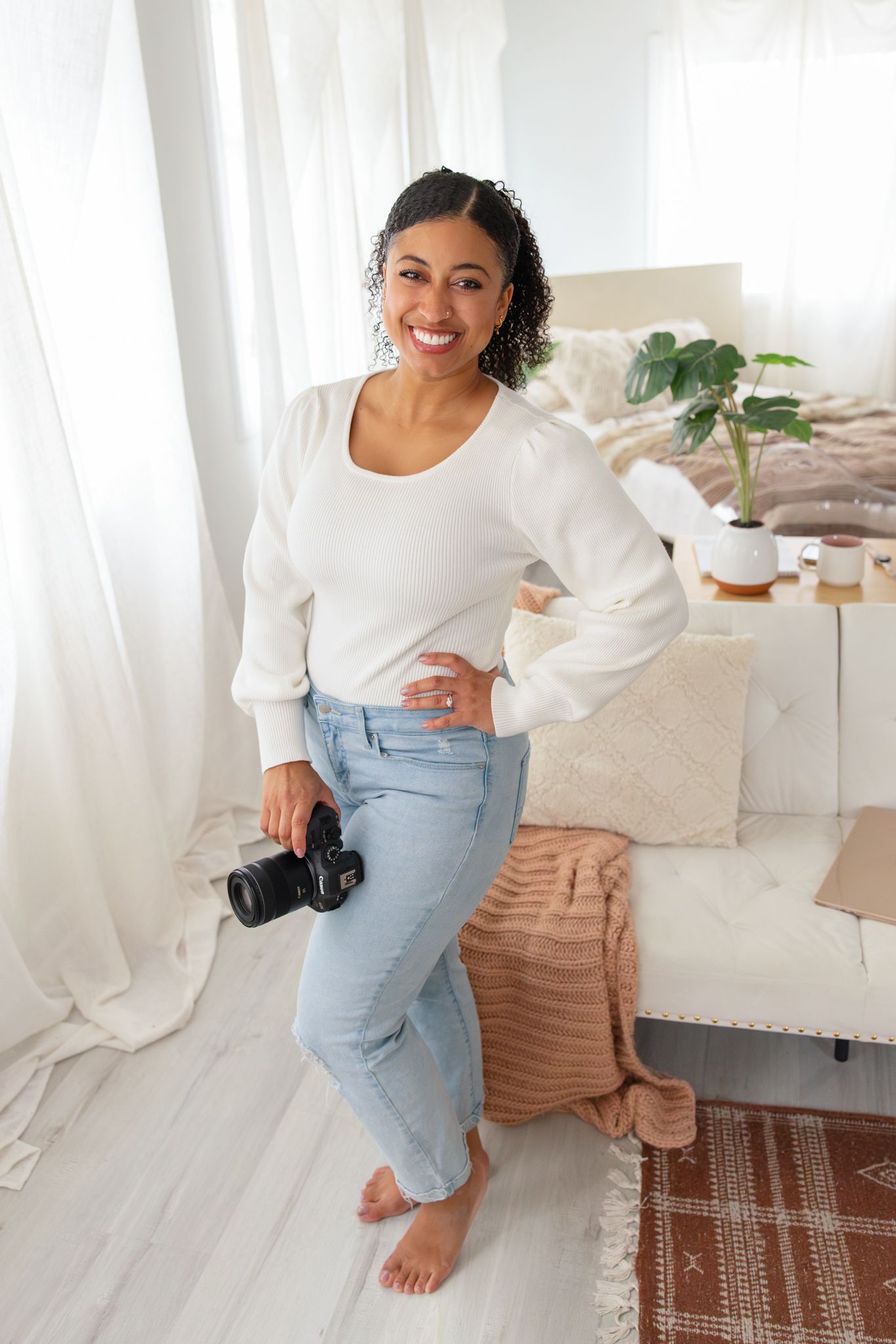 Woman wearing a pink ruffle sweater and jeans poses on a beige couch.