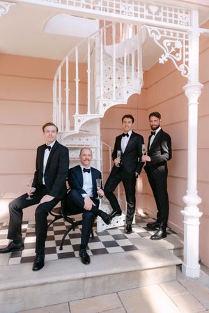 A series of four photos showing groomsmen in black tuxedos sitting on white stairs with a checkered floor pattern.