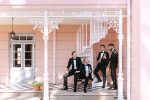 A panoramic view of a wedding party walking under a decorative white colonnade at an elegant pink venue.