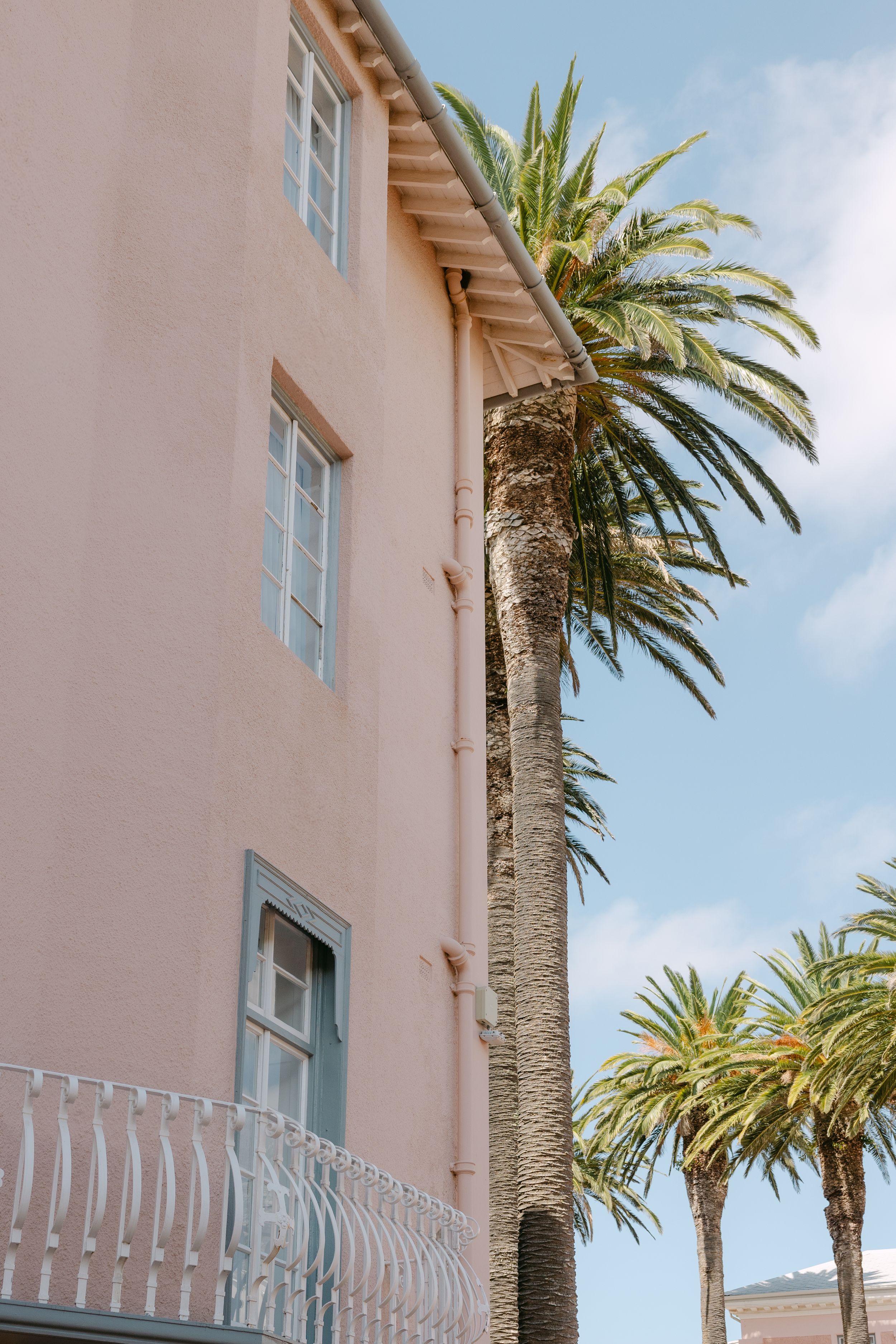 Pink stucco building exterior with tall palm trees and white balcony railings against a blue sky.