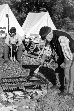 Civil War era cooking demonstration with cast iron pots over open fire at historical reenactment.
