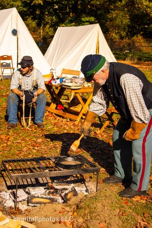 Reenactors demonstrate outdoor cooking methods at a Civil War camp with tents in background.