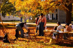 Fall scene of historical reenactment camp with golden leaves and white tents.