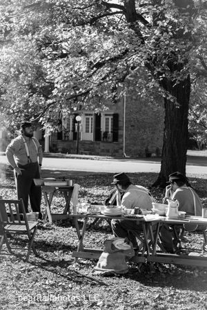 Black and white image of historical camp scene with people gathered under autumn trees.