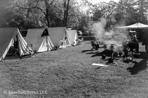 A row of white canvas tents set up in a field with smoke rising from campfires.