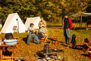 Autumn campground scene with multiple white canvas tents and reenactors in period clothing.