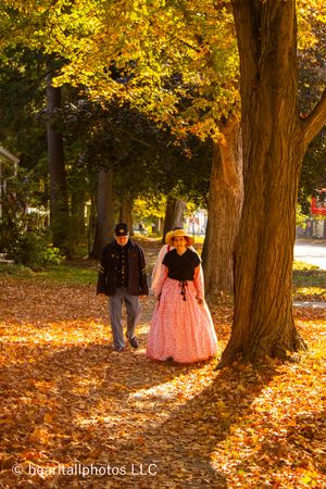Autumn sunlight illuminates golden leaves as people in historical costumes walk through a park.