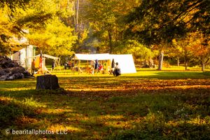 Golden autumn sunlight streams across a field with historical reenactment tents in the distance.