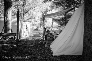 A line of white canvas tents stretches across a sunny field during a historical reenactment.
