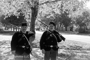 Civil War reenactors in period uniforms stand near trees during an autumn historical demonstration.