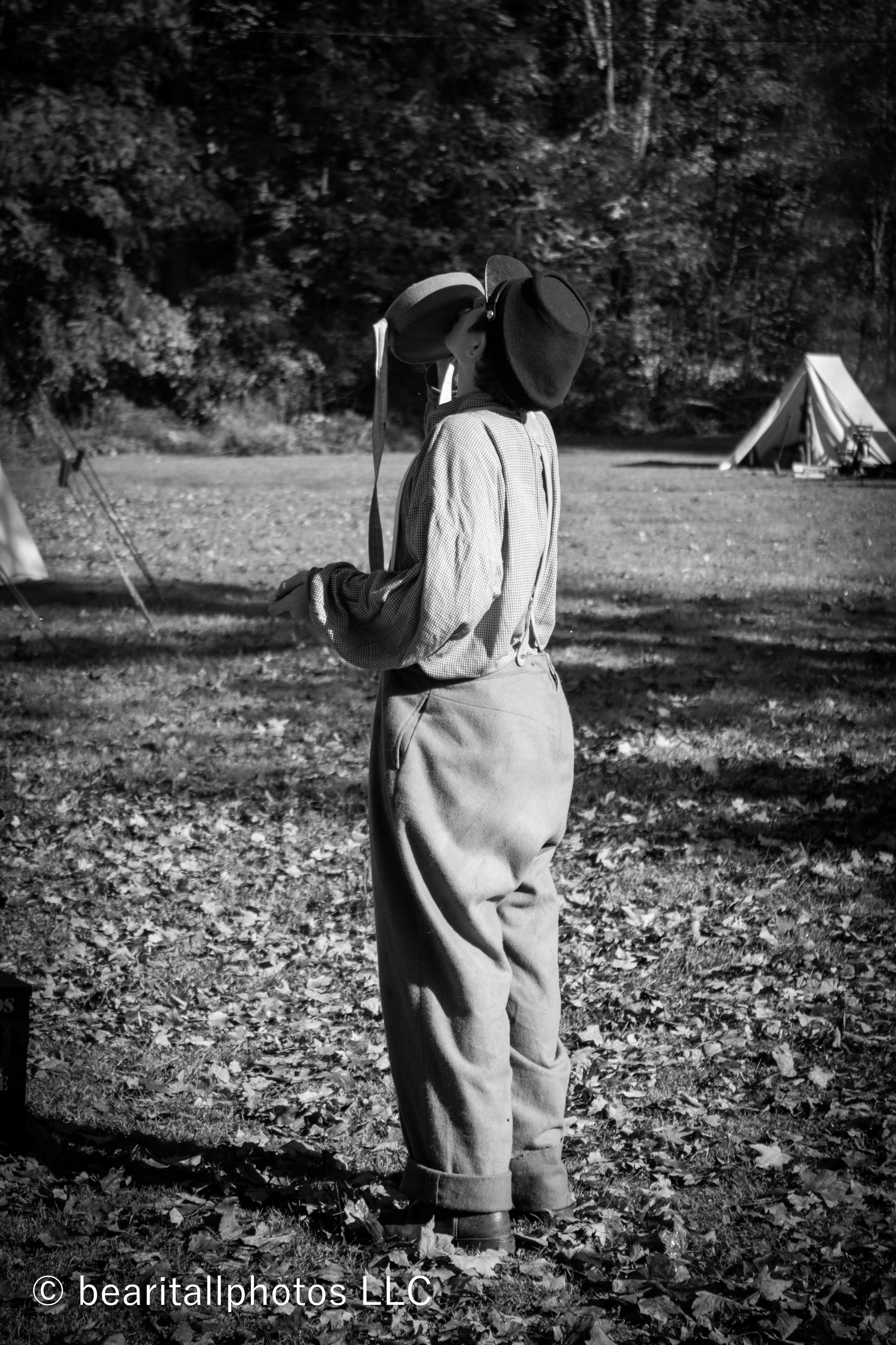 Person in period dress walking through a historical reenactment campsite with tents in background.
