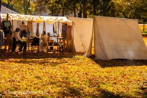 Civil War reenactment campground with white tents amid fallen autumn leaves.