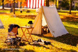 American flag flies over Civil War reenactment camp with white tents in golden autumn light.