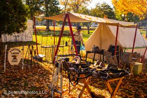 Historical camp setup with canvas tents and period furniture surrounded by autumn foliage.