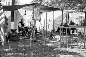 Civil War reenactment camp with canvas tents and period furnishings set up in a wooded area.