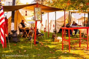 Civil War era campsite with American flags and canvas tents illuminated in warm sunlight.