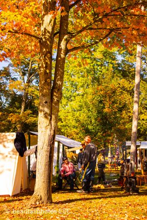 Fall foliage frames a Civil War reenactment camp with tents and participants.