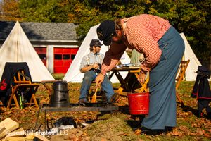 Historical reenactment camp showing people in period dress around canvas tents during fall.
